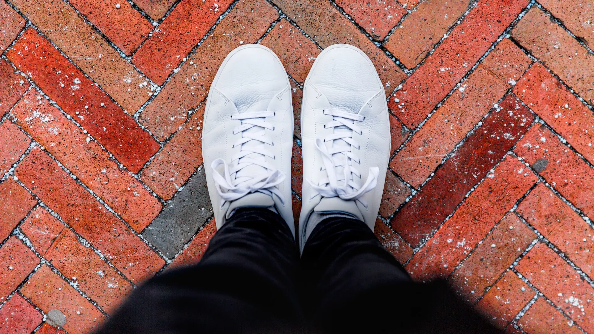 person wearing white sneakers standing on top of brown brick ground